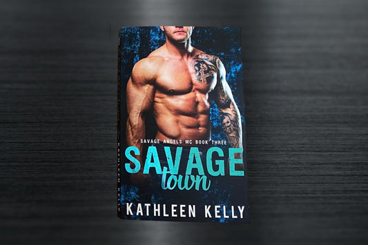 A paperback book titled 'Savage Town' with a foiled teal title on the cover, featuring an image of a man with a tattoo.